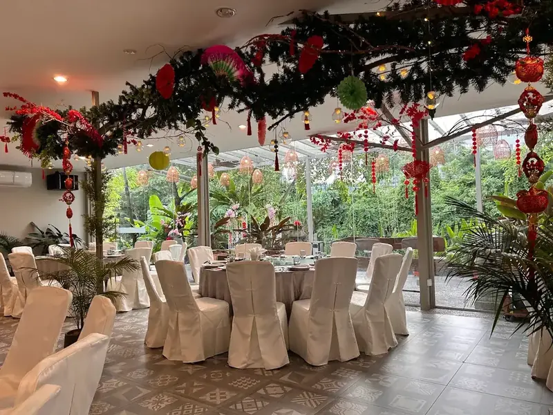 Garden dining hall with round tables, white chair covers and greenery outside the glass walls