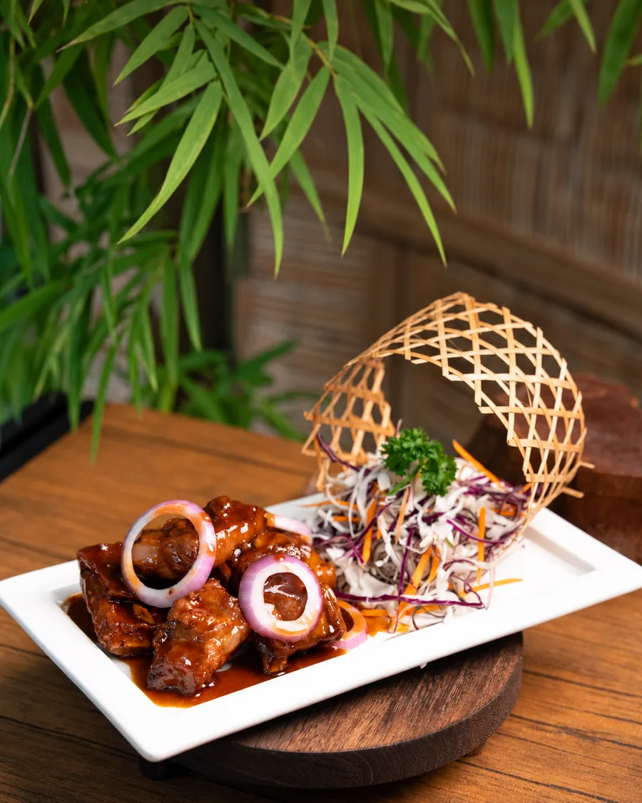 Deep-fried pork ribs with red onion rings in a glossy vinegar sauce, served with shredded cabbage on a white plate